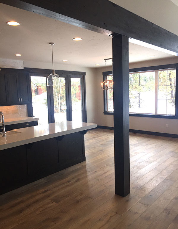 engineered hardwood flooring in new home in kitchen and living room with black cupboards and black accent beams