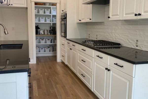 oak hardwood floors in updated kitchen with white cupboards and black countertops