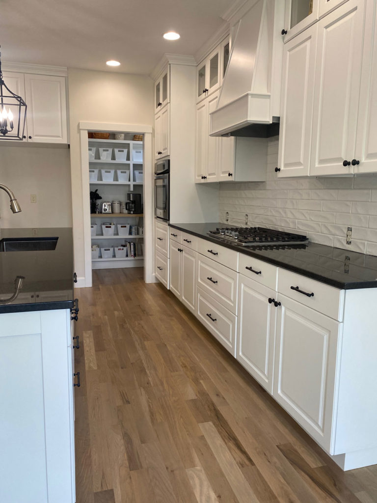 oak hardwood floors in updated kitchen with white cupboards and black countertops