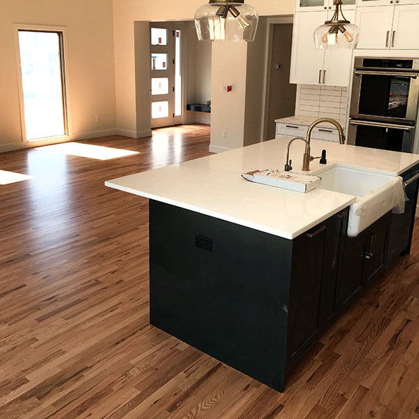 new hardwood floors in updated kitchen with black cupboards and white countertops.